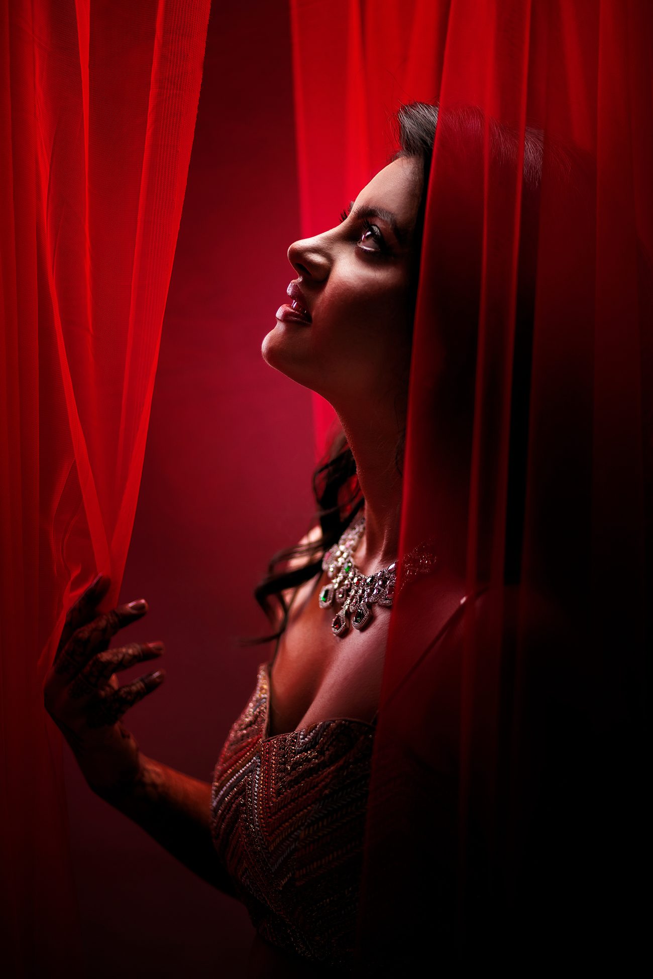 Bride glancing upward through red curtains, photographed by Mograa House
